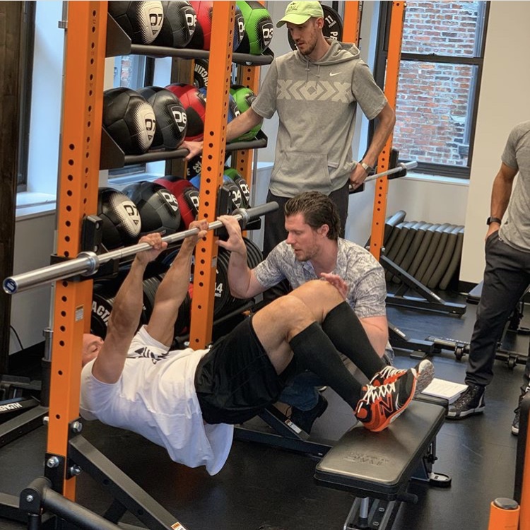 A Saint Bartholomew coach supervising a barbell strength assessment in the clinic